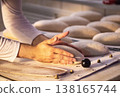 Hands of baker shaping dough for artisan bread creation in traditional bakery setting, careful preparation of fresh baked goods with flour dusting 138165744