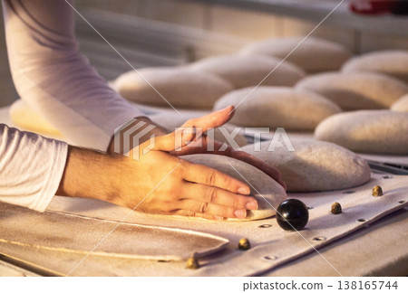 Hands of baker shaping dough for artisan bread creation in traditional bakery setting, careful preparation of fresh baked goods with flour dusting Hands of baker shaping dough for artisan bread creation in traditional bakery setting, careful preparation of fresh baked goods with flour dusting 138165744