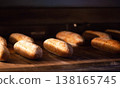 Golden brown artisanal bread loaves baking inside warm dark oven. Freshly baked rustic bread dough cooking to perfection, creating delicious bakery product. 138165745