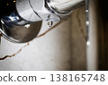 Water droplet forming on underside of polished chrome heated towel rail, water drip against blurred bathroom wall background, close-up shot of water leak. Copy space for text 138165748