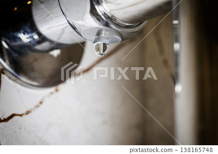Water droplet forming on underside of polished chrome heated towel rail, water drip against blurred bathroom wall background, close-up shot of water leak. Copy space for text 138165748