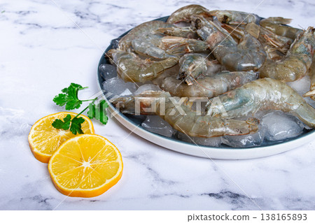 Fresh raw shrimp spread on ice with lemon and cilantro slices on a marble surface, ready to cook, no people Fresh raw shrimp spread on ice with lemon and cilantro slices on a marble surface, ready to cook, no people 138165893