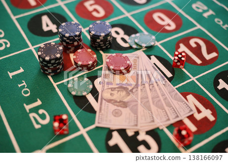 Excitement builds as chips stack and money lays before players at the lively roulette table under bright casino lights Excitement builds as chips stack and money lays before players at the lively roulette table under bright casino lights 138166097