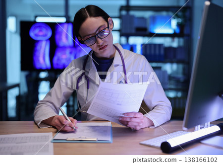 Focused medical professional examines patient data while working in a modern, illuminated healthcare setting Focused medical professional examines patient data while working in a modern, illuminated healthcare setting 138166102