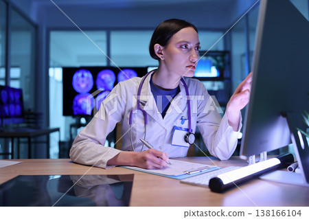 Focused medical professional analyzes patient data while working late in a modern health facility 138166104