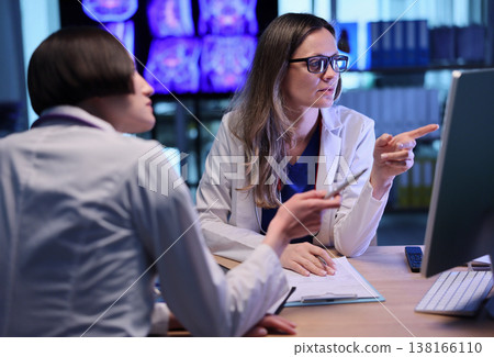 Two doctors collaborate in a modern workspace, discussing patient data and brain scans in a bright, high-tech environment Two doctors collaborate in a modern workspace, discussing patient data and brain scans in a bright, high-tech environment 138166110