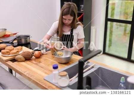 Young chef prepares delicious dish in modern kitchen during sunny afternoon while family enjoys baking together 138166121