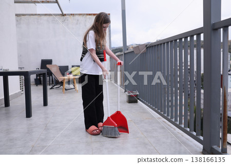 Young girl sweeping a balcony on a cloudy afternoon while showcasing her determination and a sense of responsibility Young girl sweeping a balcony on a cloudy afternoon while showcasing her determination and a sense of responsibility 138166135