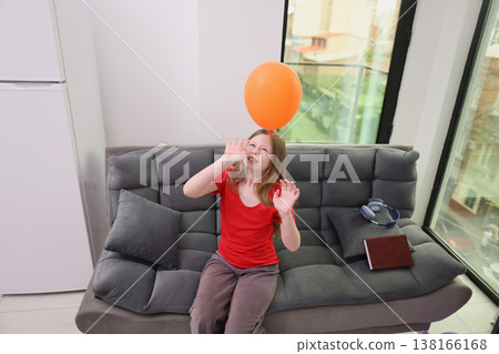 Joyful moments filled with laughter as a child plays with a bright orange balloon in a sunny living room 138166168