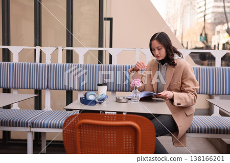 Woman enjoying a cozy moment reading a magazine while sipping coffee in a stylish outdoor cafe on a sunny day in the city 138166201