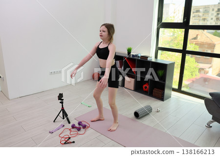 Young girl practices fitness routines in a bright cozy room filled with workout equipment and sunlight streaming through the window 138166213