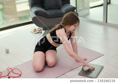 Young girl engaged in an online workout session in a modern home studio with natural light streaming through the windows 138166216