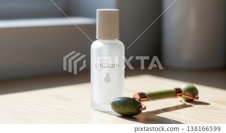 Minimalist shot of a frosted glass collagen serum bottle next to a green jade face roller on a wooden surface in soft sunlight. 138166599