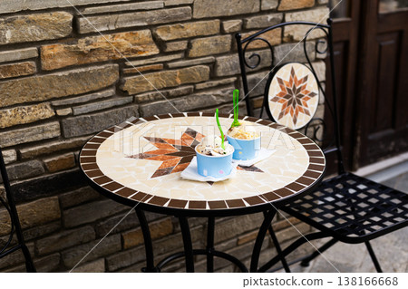 Two paper cups filled with delicious ice cream scoops sitting on a table at an outdoor summer cafe. Refreshing street food concept with blurred background and copy space Two paper cups filled with delicious ice cream scoops sitting on a table at an outdoor summer cafe. Refreshing street food concept with blurred background and copy space 138166668