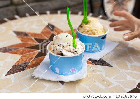 shot of creamy gelato in small paper containers on a textured mosaic surface. Summer vacation aesthetic with outdoor terrace seating and rich colors 138166670