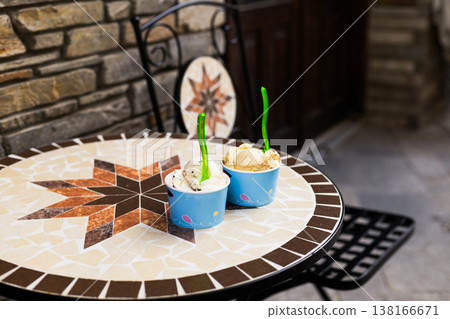 Gelato in disposable eco friendly paper cups placed on a cafe terrace table. Summer outdoors lifestyle featuring sweet cold dessert and natural daylight Gelato in disposable eco friendly paper cups placed on a cafe terrace table. Summer outdoors lifestyle featuring sweet cold dessert and natural daylight 138166671