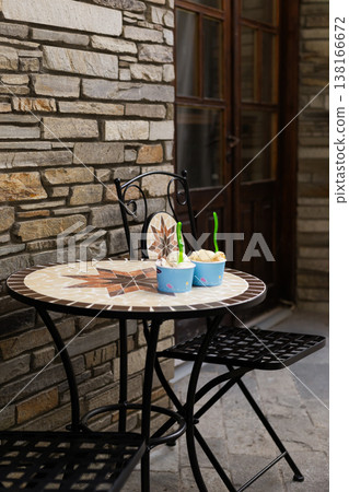 Pair of colorful ice cream portions in paper bowls on a table outside a coffee shop. Tasty summer treat enjoyed outdoors during a warm sunny day 138166672