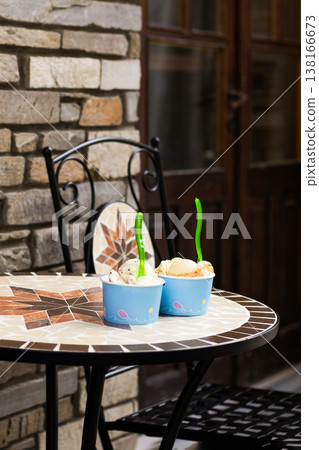 Two paper cups of scooped ice cream on an urban metal table against a classic red brick wall background. City street food style and industrial cafe terrace concept 138166673