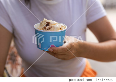 Close up of female hands holding a refreshing gelato cup against a clean white t shirt background. Minimalist summer food aesthetic with empty space on clothing for mockup Close up of female hands holding a refreshing gelato cup against a clean white t shirt background. Minimalist summer food aesthetic with empty space on clothing for mockup 138166680