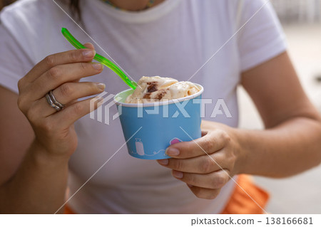 Unrecognizable young woman wearing a casual white t shirt holding a paper cup with an ice cream scoop. Summer lifestyle portrait focusing on female hands and sweet frozen dessert Unrecognizable young woman wearing a casual white t shirt holding a paper cup with an ice cream scoop. Summer lifestyle portrait focusing on female hands and sweet frozen dessert 138166681