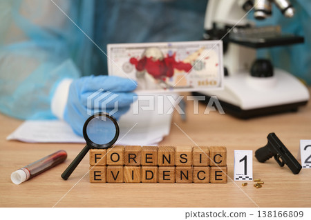 Forensic lab scene with evidence collection involving a mock crime setup featuring blood-stained currency and a firearm 138166809
