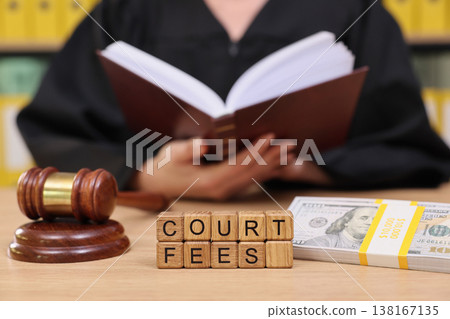 Gavel and court fees in a courtroom setting with a judge reading from a legal book during a judicial session Gavel and court fees in a courtroom setting with a judge reading from a legal book during a judicial session 138167135