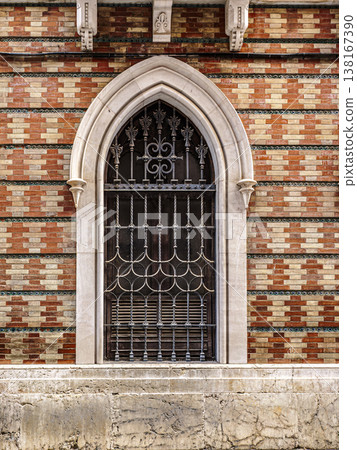 Gothic Arched Window With Decorative Iron Grille and Stone Surround in Patterned Brick Fa?ade Gothic Arched Window With Decorative Iron Grille and Stone Surround in Patterned Brick Fa?ade 138167390
