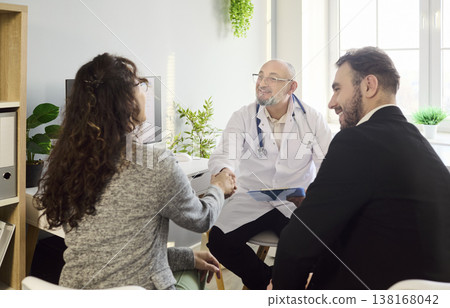 Smiling doctor greeting couple with handshake during consultation in clinic office Smiling doctor greeting couple with handshake during consultation in clinic office 138168042