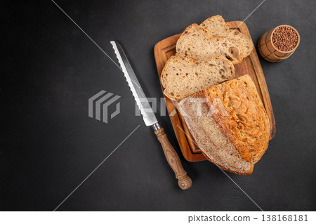 Seeded bread loaf with slices and knife on dark background top view Seeded bread loaf with slices and knife on dark background top view 138168181