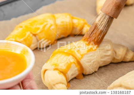 Raw croissant brushed with egg wash on baking paper, close-up pastry preparation process 138168187