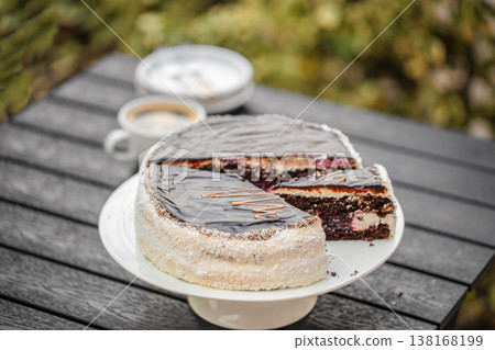 Chocolate cake with slice on stand and coffee on outdoor table Chocolate cake with slice on stand and coffee on outdoor table 138168199