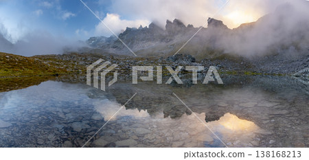 Mist rises over a serene Wildsee lake in the Pizol mountains at sunrise, casting a mystical atmosphere. The rocky terrain and clear waters reflect the early morning light Mist rises over a serene Wildsee lake in the Pizol mountains at sunrise, casting a mystical atmosphere. The rocky terrain and clear waters reflect the early morning light 138168213