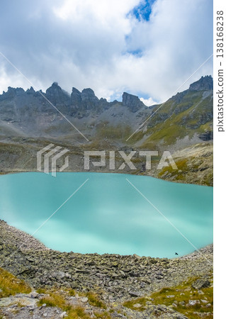 Captivating landscape of Pizol Wildsee lake in the Swiss Alps, featuring tranquil turquoise water amid rugged peaks enveloped by mist and clouds, creating a dramatic mountain scene 138168238