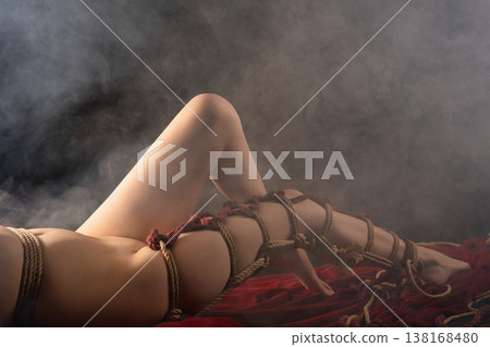 Sensual cropped view of a body bound in artistic Shibari ropes lying on red fabric 138168480