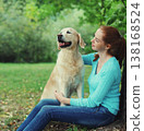 Happy owner woman with Golden Retriever dog sitting in summer park 138168524