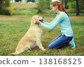 Happy owner woman with Golden Retriever dog sitting on grass together in park 138168525