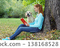 Happy owner woman reading book with dog sitting in summer park 138168528