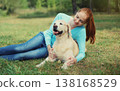 Happy owner woman with Golden Retriever dog sitting on grass together in park 138168529