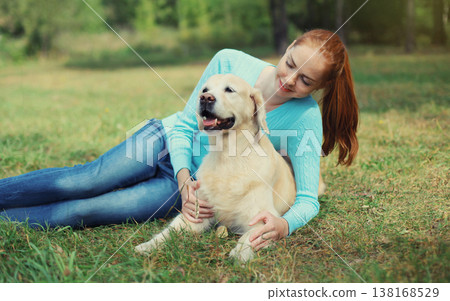 Happy owner woman with Golden Retriever dog sitting on grass together in park Happy owner woman with Golden Retriever dog sitting on grass together in park 138168529
