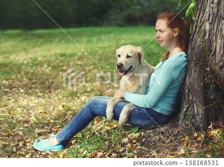 Happy owner woman with Golden Retriever dog sitting in summer park Happy owner woman with Golden Retriever dog sitting in summer park 138168531