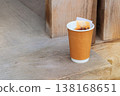 Black tea takeaway. Paper cup with tea bag on a wooden background. Breakfast break.  One-use drinkware. 138168651