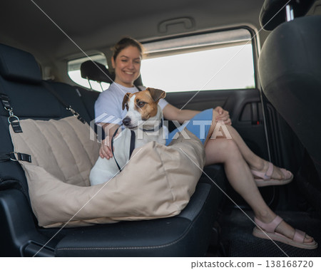 Caucasian woman travels by car with her dog. Jack Russell Terrier in a special car seat. Caucasian woman travels by car with her dog. Jack Russell Terrier in a special car seat. 138168720