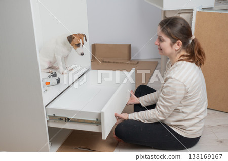 A Caucasian woman assembles furniture with her cute dog. A Caucasian woman assembles furniture with her cute dog. 138169167
