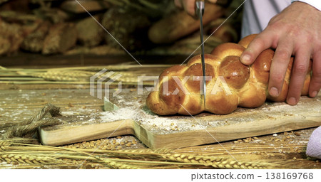 Fresh bread is sliced with a knife on a wooden board in a kitchen setting during the daytime Fresh bread is sliced with a knife on a wooden board in a kitchen setting during the daytime 138169768