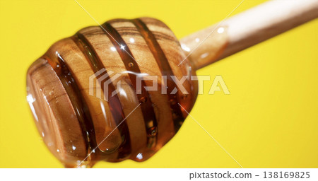 Close-up view of honey dripping from wooden dipper against yellow background showing natural sweetness Close-up view of honey dripping from wooden dipper against yellow background showing natural sweetness 138169825