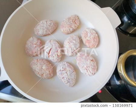 Raw breaded meat cutlets or patties arranged in a white frying pan with oil, ready to be cooked Raw breaded meat cutlets or patties arranged in a white frying pan with oil, ready to be cooked 138169971