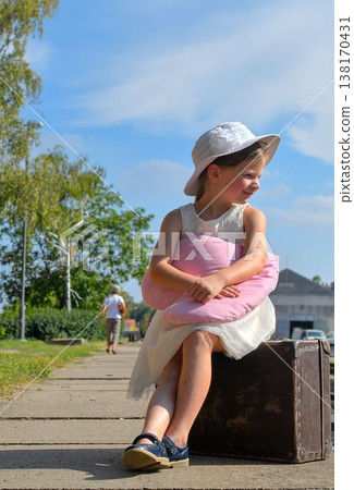 A cute girl at the train station. A little girl holds a plush toy and sits on an old suitcase. The concept of travel, vacations, and a carefree childhood. Retro and vintage vibes. 138170431