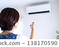 一手拿著空調遙控器調節溫度。這張圖象徵著為應對電價飆升和能源短缺而採取的措施。 138170590