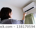 一手拿著空調遙控器調節溫度。這張圖象徵著為應對電價飆升和能源短缺而採取的措施。 138170594