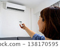 一手拿著空調遙控器調節溫度。這張圖象徵著為應對電價飆升和能源短缺而採取的措施。 138170595